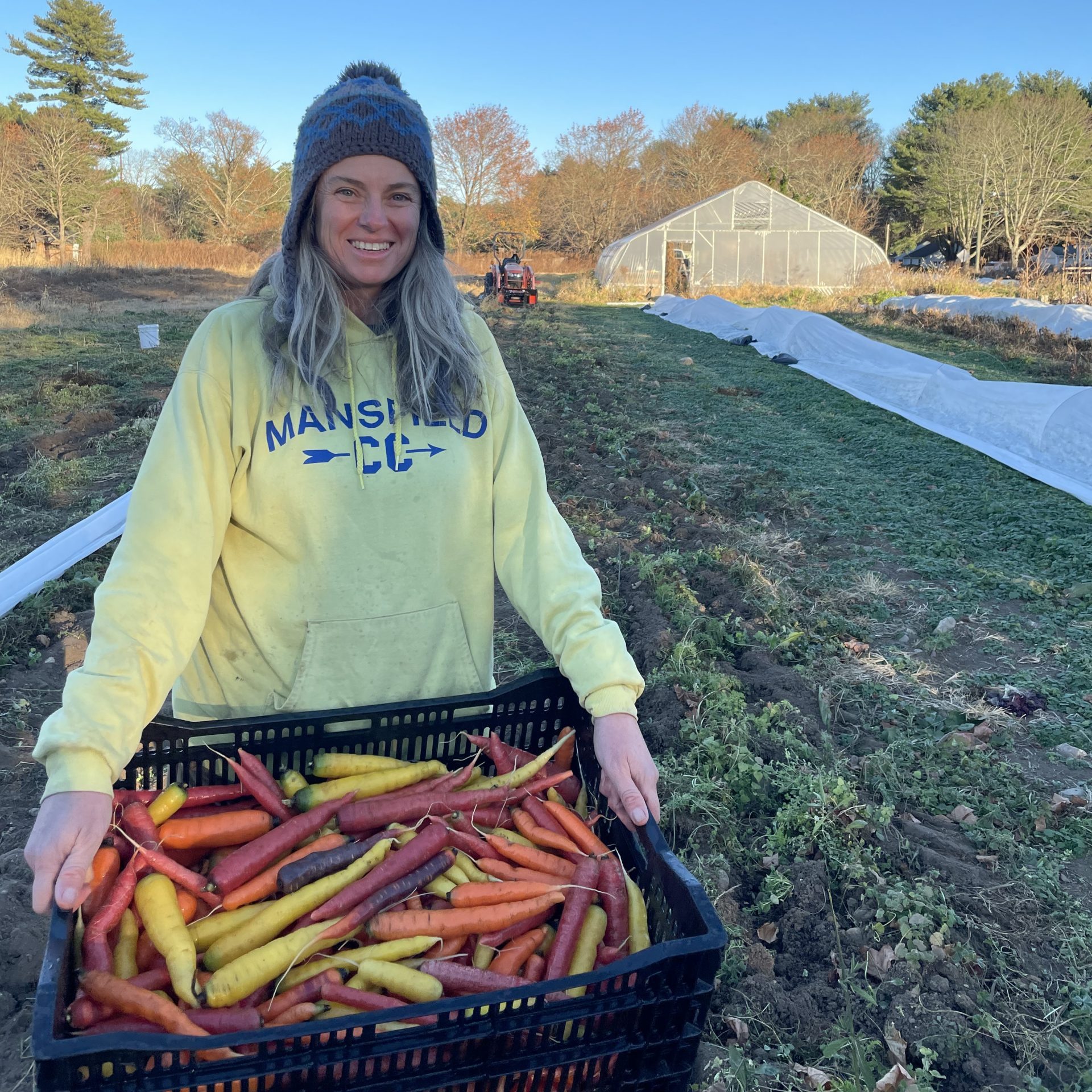 Diane holding a crate of veggies in a field